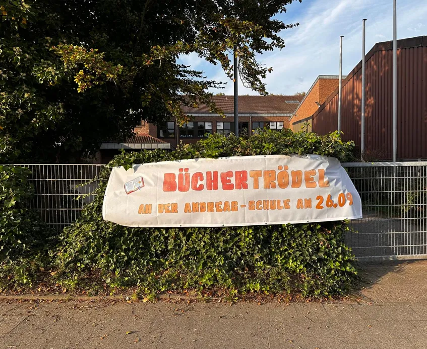 Das Plakat mit der Einladung Büchertrödel am 26.09. ziert den Zaun der Andreas-Schule.